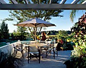 VIEW ACROSS DECKED VERANDAH WITH SIX CANVAS CHAIRS AND PARASOL. BILL SMITH AND DENNIS SCHRADERS GARDEN  LONG ISLAND  USA