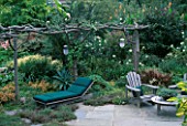 UNUSUAL PERGOLA MADE FROM NATURAL TIMBER STANDS OVER GREEN CANVAS SUN LOUNGER AND WOODEN GARDEN FURNITURE. BILL SMITH AND DENNIS SCHRADERS GARDEN  LONG ISLAND  USA