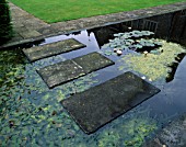 STONE SLABS FORM A STEPPING STONE BRIDGE OVER A FORMAL WATER GARDEN PLANTED WITH WATERLILIES. DENMANS GARDEN  DESIGNER JOHN BROOKES