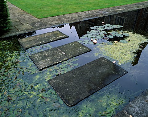 STONE_SLABS_FORM_A_STEPPING_STONE_BRIDGE_OVER_A_FORMAL_WATER_GARDEN_PLANTED_WITH_WATERLILIES_DENMANS