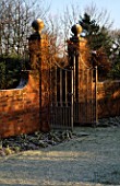 WINTER SUNLIGHT SHINES ON THE ORNATE METAL GATES WHICH DIVIDE THE FROST COVERED GARDEN AT WOLLERTON OLD HALL  SHROPSHIRE.