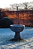 WINTER SUNLIGHT SHINES THROUGH THE BEECH HEDGES ONTO AN OLD STONE URN IN THE FROSTED GARDEN. WOLLERTON OLD HALL  SHROPSHIRE.
