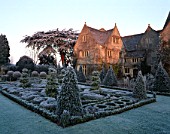 VIEW ACROSS THE FROSTED CELTIC KNOT GARDEN WITH TOPIARY  TOWARDS THE SUNLIT HOUSE. THE ABBEY HOUSE  WILTSHIRE.
