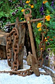 RUSTY ANCHOR NEXT TO DRIFTWOOD BENCH WITH PATTERNED GRAVEL FLOOR  VIOLAS & MARIGOLDS.  WARREN FARM CENTRES THE ESSENCE OF LIFE  GARDEN. DES: ROSAMOND PAGE  CHELSEA 2000