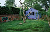 THE CHILDRENS PLAY AREA WITH BLUE SUMMERHOUSE  BLACKBOARD  HAMMOCK  TURF CROCODILE AND OLD TREE. DESIGN BY CLARE MATTHEWS