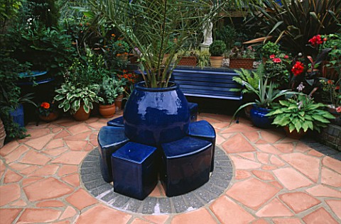 SOFT_TERRACOTTA_CRAZY_PAVING_PATIO_WITH_BLUE_CERAMIC_SEATS_AND_TRACHYCARPUS_FORTUNEI_ROBIN_GREEN__RA