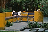 A PLACE TO SIT: ALUMINIUM TABLE AND CHAIRS ON PATIO SURROUNDED BY YELLOW RENDERED WALLS WITH RAISED BEDS AND RILL WITH OLEANDER   TRACHYCARPUS. DESIGNER JOE SWIFT