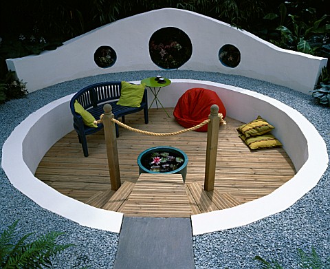 A_CIRCULAR_SUNKEN_TIMBER_DECK_PATIO_AREA_WITH_BEANBAG__GLAZED_POT_WITH_WATERLILY_AND_BLUE_SEAT_HAMPT