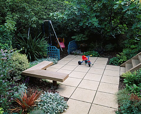 CHILDRENS_GARDEN_SWINGS_WITH_BARK_BENEATH__BLUE_TRELLIS_SCREENS__PAVING__WOODEN_SEAT__PHORMIUM_AND_F