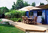 BLUE SUMMERHOUSE WITH DECKING  TABLE  CHAIRS  PARASOL AND GRAVEL. DESIGNER: CLARE MATTHEWS