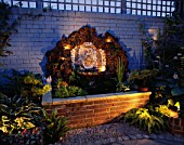 WATER FEATURE: RECTANGULAR BRICK POOL WITH SHELL WALL FOUNTAIN BACKED BY ROCK AND BRICK WALL PAINTED BLUE  LIT UP AT NIGHT. DESIGNER: ANDREW ANDERSON