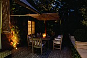 DECKED TERRACE WITH WOODEN TABLE  CHAIRS AND PARASOL  LIT UP AT NIGHT WITH CANDLES AND LIGHTS: LIGHTING BY GARDEN AND SECURITY LIGHTING