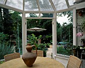 TABLE AND CHAIRS IN CONSERVATORY WITH VIEW OF LISETTE PLEASANCES GARDEN OUTSIDE