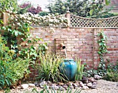 GRAVEL COURTYARD WITH WATER FEATURE: BRICK WALL  TRELLIS  WATER SPOUT   TURQUOISE CONTAINER  ROCKS AND CLEMATIS MONTANA