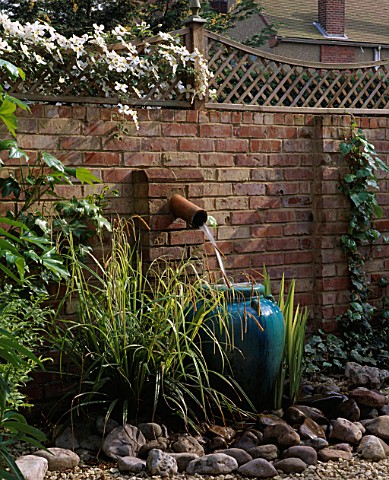 GRAVEL_COURTYARD_WITH_WATER_FEATURE_BRICK_WALL__TRELLIS__WATER_SPOUT___TURQUOISE_CONTAINER__ROCKS_AN
