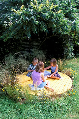 JASMINE__ANDY_AND_SHANA_HICKS_SIT_ON_THE_YELLOW_CIRCLE_OF_DECK_SURROUNDED_BY_RHUS_TYPHINA__BIDENS_AU