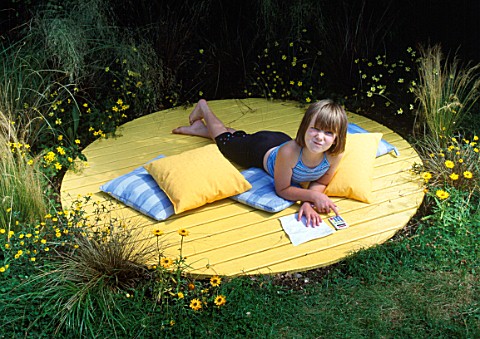 SHANA_HICKS_RELAXES_ON_THE_YELLOW_DECK_CIRCLE_SURROUNDED_BY_RHUS_TYPHINA__BIDENS_AUREA__HELICHRYSUM_