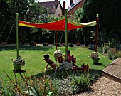 SHADE CANOPY: JOSHUA AND NANCY RELAX I N DECKCHAIRS UNDERNEATH THE SHADE CANOPY ON THE LAWN: DESIGNER: CLARE MATTHEWS