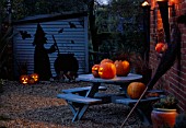 HALLOWEEN: GRAVEL COURTYARD WITH BLUE TABLE  PUMPKINS  BESOM BROOM  BLUE SHED WITH WITCH AND COULDRON SILHOUETTE CUT FROM PVC PONDLINER