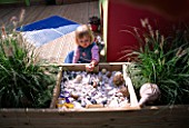CHILDRENS DECK GARDEN: LUCY FEELING THE SHELLS  FIR CONES AND STONES IN A RAISED WOODEN BED