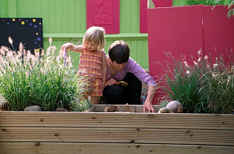 CHILDRENS_DECK_GARDEN_LUCY_AND_RACHAEL_PLAY_IN_THE_RAISED_WOODEN_BED_THE_GRASS_IS_PENNISETUM_HAMELYN