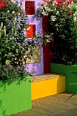 THE SPECSAVERS GARDEN: CONCRETE RENDERED WALL PAINTED MAUVE WITH COLOURED WINDOWS AND WOODEN BENCH. DESIGNERS NAILA GREEN AND LEE JACKSON