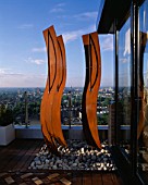 AFRICAN THEMED ROOF TERRACE: THREE CORE-TEN STEEL AFRICAN SHIELDS  FRAMEWORK OF PEBBLES   COPPER UPLIGHTERS  GLASS BALUSTRADE AND IROKO DECKING.  DESIGN: S. WOODHAMS