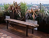 AFRICAN THEMED ROOF TERRACE: A PLACE TO SIT: RAILWAY SLEEPER BENCH  GLASS BALUSTRADE   CONTAINERS WITH PHORMIUM TENAX RAINBOW QUEEN & P.PLATTS BLACK. DESIGN: S. WOODHAMS