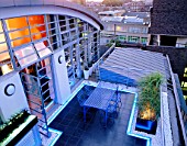 ROOF GARDEN DESIGNED BY STEPHEN WOODHAMS LIT UP AT NIGHT: BLACK SLATE TERRACE WITH TABLE AND CHAIRS AND NEON STRIP LIGHTING ON THE FIFTH FLOOR