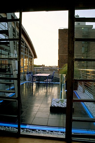 VIEW_OUT_OF_FLAT_ONTO_BLACK_SLATE_TERRACE_WITH_METAL_TABLE_AND_CHAIRS_AND_WATER_FEATURE_NEON_STRIP_L