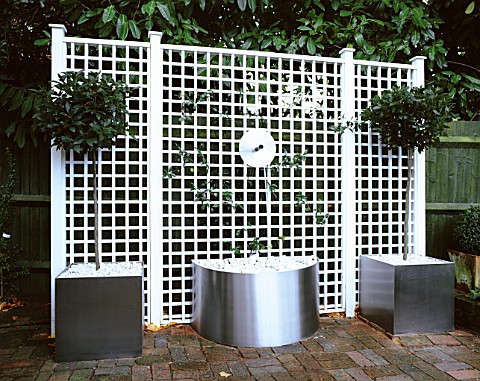 WATER_FEATURE_STAINLESS_STEEL_DISC_AND_SPOUT_POURS_INTO_CONTAINER_WITH_WHITE_PEBBLES_WHITE_TRELLIS_B