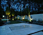THE SANCTUARY GARDEN  CHELSEA 2002  LIT UP AT NIGHT. DESIGNER: STEPHEN WOODHAMS: LIMESTONE TERRACE  LAWN  CLIPPED CARPINUS BETULUS  WATER FEATURE. 5 FACE SCULPTURE BY STEPHEN COX