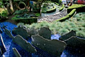 HELTER SKELTER   GARDEN CREATED BY TONY HEYWOOD OF CONCEPTUAL GARDENS  LONDON: FESTUCA GLAUCA  SLATE  BLUE GRAVEL  ROCKS AND A POLISHED MARINE STEEL CURVED MIRROR