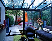VIEW OUT OF FLAT WITH PINK WOODEN TABLE  ORANGE PARASOL  DECKING & ORANGE CANNAS: DESIGNER: STEPHEN WOODHAMS. CONSERVATORY  GLASS  SUNROOM  INTERIOR