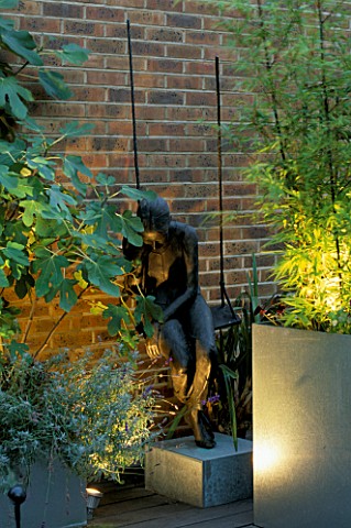 CORNER_OF_ROOF_GARDEN_LIT_UP_AT_NIGHT_WITH_DECKING__FIG_AND_BAMBOO_IN_GALVANISED_CONTAINER_AND_GIRL_