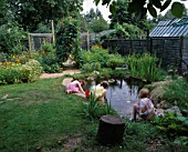 CHILDREN PLAYING BESIDE THEWILDLIFE POND IN ROSEMARY PEARSONS GARDEN  READING  WITH THE POTAGER IN THE BACKGROUND
