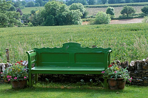 OLD_GREEN_BENCH_ON_LAWN_WITH_WHEATFIELD_BEHIND_LAUNA_SLATTERS_GARDEN__OXFORDSHIRE