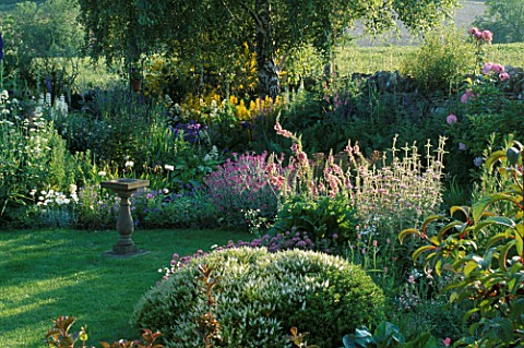 LAUNA_SLATTERS_GARDEN_OXFORDSHIRE_BORDER_BESIDE_POND_WITH_LAWN_AND_SUNDIAL__PLANTED_WITH_HEBE_RAKAIE