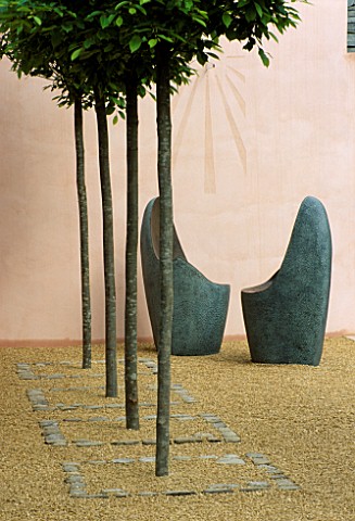 TWO_ROUNDED_METAL_SEATS_IN_FRONT_OF_PINK_WALLS_WITH_SUNDIAL_IN_LLADROS_SENSUALITY_GARDEN_ROW_OF_CLIP