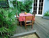 SMALL TOWN GARDEN WITH DECKING  PAVING  TABLE AND CHAIRS AND TRACHYCARPUS FORTUNEI. DESIGNER: SARAH LAYTON