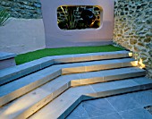 SMALL COURTYARD WITH STEPS AND RENDERED CONCRETE APERTURE WITH SCULPTURE  LIT UP AT NIGHT. DESIGNER: AMIR SCHLEZINGER/MY LANDSCAPES
