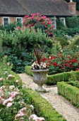 THE PRIORY  BEECH HILL  BERKSHIRE: THE NEW ROSE PARTERRE WITH BOX EDGING  STONE URN WITH PHORMIUM AND WHITE BEGONIAS  WOODEN ARCH PLANTED WITH AN AMERICAN PILLAR ROSE