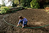CLARE MATTHEWS USING A HOSE PIPE TO LAY OUT A PATH IN HER DEVON GARDEN