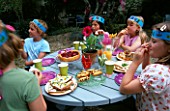 DESIGNER CLARE MATTHEWS: CHILDRENS PARTY - CHILDREN ENJOYING A PARTY TEA ON A BLUE WOODEN TABLE IN THE GRAVEL GARDEN