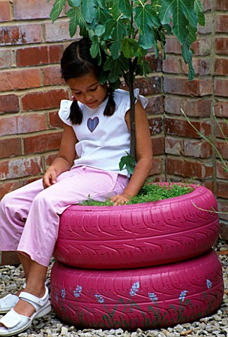 DESIGNER_CLARE_MATTHEWS__FRAGRANT_TREE_SEAT__GIRL_SITTING_ON_PINK_PAINTED_CAR_TYRES_PLANTED_WITH_A_F