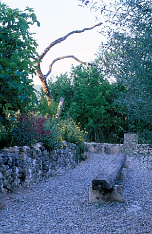 LA_CHABAUDE__FRANCE_DESIGNER__PHILIPPE_COTTET_GRAVEL_TERRACE_WITH_LARGE_WOODEN_LOG_SEAT__STONE_WALL_
