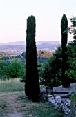 LA CHABAUDE  FRANCE. DESIGNER - PHILIPPE COTTET:VIEW OUT OF GARDEN TO COUNTRYSIDE BEYOND WITH PENCIL CYPRESS AND STONE WALL