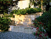 LA CHABAUDE  FRANCE. DESIGNER - PHILIPPE COTTET: STONE WATER FEATURE ON GRAVEL TERRACE WITH CENTRANTHUS RUBER