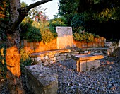 LA CHABAUDE  FRANCE. DESIGNER - PHILIPPE COTTET: STONE AND WOOD SEATING AREA ON GRAVEL TERRACE WITH PINE TREE
