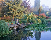 VIEW ACROSS THE LILY POND WITH A WOODEN PONTOON  ROCK SCULPTURES AND AN AGAVE IN A CONTAINER. DESIGNER: JOHN MASSEY